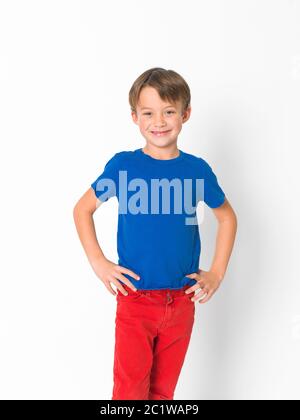 cool and cute six year old boy in red trousers and blue shirt is posing in front of white background Stock Photo