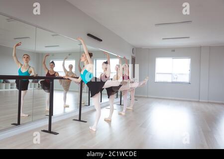 Caucasian female attractive ballet dancers stretching out and holding a barre in a bright studio Stock Photo