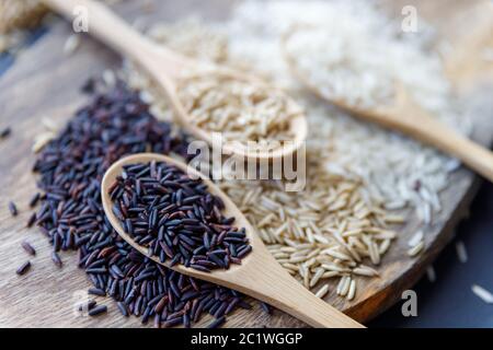 Black wild rice, brown wild rice and white jasmine rice in wooden spoon flat lay. Creative layout. Food concept. Focus on black rice. Stock Photo
