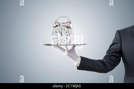 Businessman offering old style alarm clock on silver tray Stock Photo