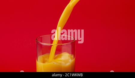 Orange juice pouring into glass, isolated on red color background, with copy space Stock Photo