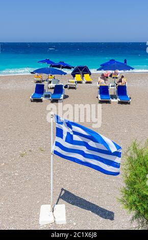 Greek flag in front of sun loungers on Rhodes Town beach, Rhodes Island, Greece Stock Photo