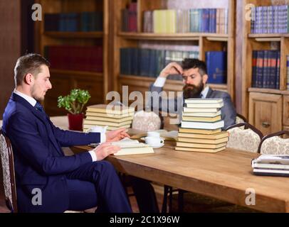 Men in suits, aristocrats, professors in library or vintage interior with bookshelves on background. Men with busy faces reading books, studying. Intellectuals and aristocrats concept. Stock Photo