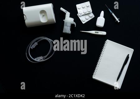 top view of nebulizer, pills, thermometer and notebook on black background Stock Photo