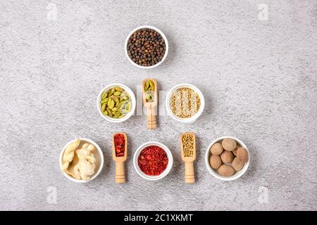 mix of aromatic spices coriander, black pepper, bergamot, dried ginger, nutmeg, paprika in white cups on gray concrete background Top view Flat lay Stock Photo