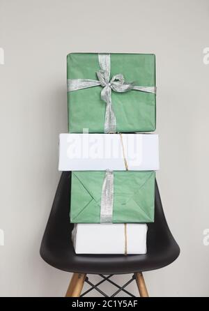 Green and white Christmas gift boxes with red ribbons on chair by the grey wall Stock Photo