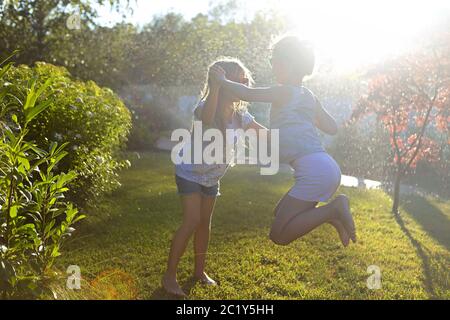 Child playing with garden sprinkler. Kids run and jump. Summer outdoor water fun in the backyard. Children play with hose wateri Stock Photo