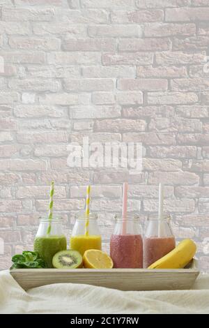 colorful fruit smoothies in a row with fresh fruits in front of a wall Stock Photo