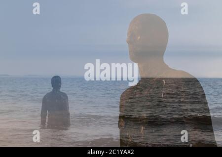 A double exposure created in camera of two Iron Men statues on the beach at Crosby, near Liverpool in England seen in June 2020. Stock Photo