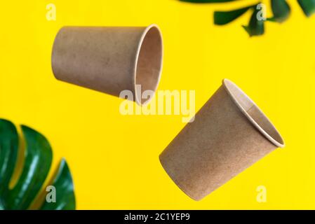 Floating eco friendly paper disposable mockup cups above yellow background with green palm leaves. Zero waste Stock Photo
