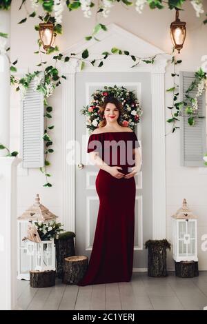 Charming pregnant woman in marsala dress posing on steps of house. Stock Photo