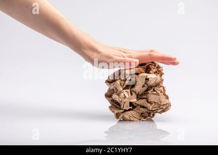 Close-up of a white people's hand crushing a crumpled piece of brown paper in front of a white background Stock Photo