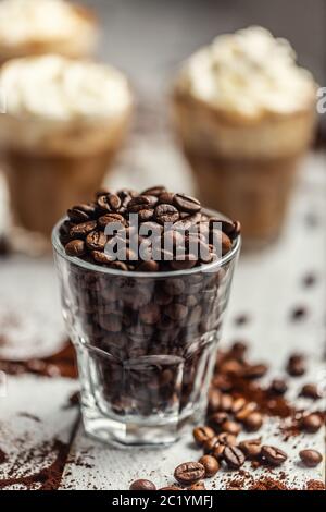 Coffee beans in a glass cup and in the background a cup with coffee and whipped cream Stock Photo