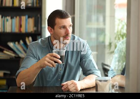 Pensive man looking away throw window holsing glass sitting in a coffee shop table Stock Photo