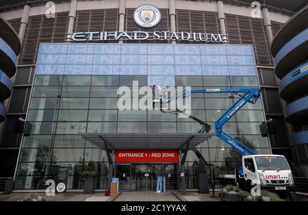 Workmen place signs outside the main entrance to the Etihad Stadium, home of Manchester City. The Premier League restarts tomorrow night with Aston Villa v Sheffield United and Manchester City v Arsenal. Stock Photo