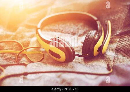 Large yellow headphones with a microphone and a long wire lie on a soft plaid blanket on the bed, illuminated by bright sunlight. Stock Photo