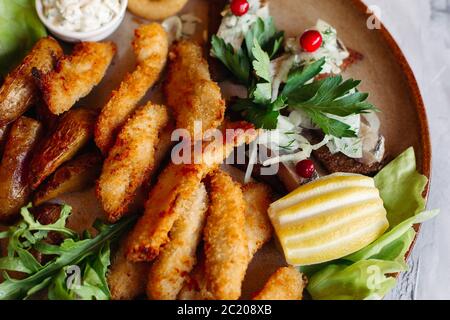 Clay plate full of delicious appetizers standing on white surface. Stock Photo