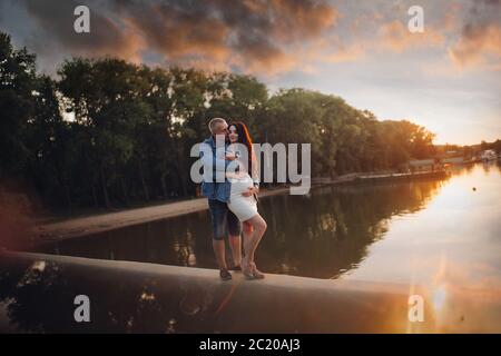 Family waiting for a baby standing by the river at sunset. Stock Photo