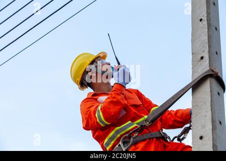 Uniformed electricians work on high-rise electricity poles along with safety equipment and using radio to control their work. Stock Photo