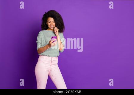 Portrait of inspired dreamy afro american girl use smart phone text type blog post think comments nail bite wear striped shirt pink pants trousers Stock Photo