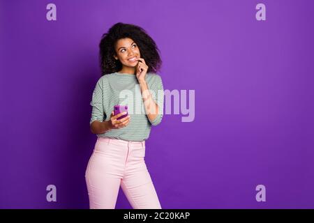 Portrait of brown curly hair afro american girl use her cell phone think thoughts social network comments feedback wear striped shirt pants pink Stock Photo