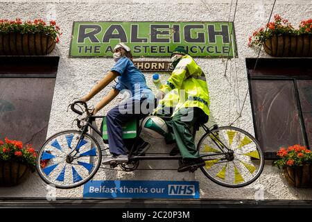 Two mannequins dressed as a nurse and an ambulance worker on a tandem bike on the wall opposite The Duke of York Bar, on Commercial Court in Belfast where the bar owner has dressed to show support for the NHS. Stock Photo