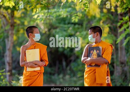 Novice monk wearing mask social distancing and enjoying with friend new normal affected from Coronavirus or Covid-19 Stock Photo