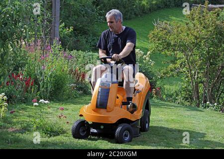 A man mows the lawn with a ride-on lawnmower. Mowing the lawn in summer Stock Photo