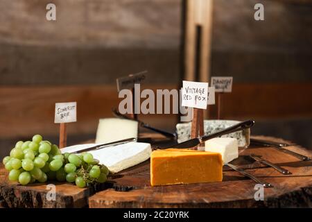 Rustic cheese board with a selection of labelled cheeses and cured meats with grapes. Stock Photo