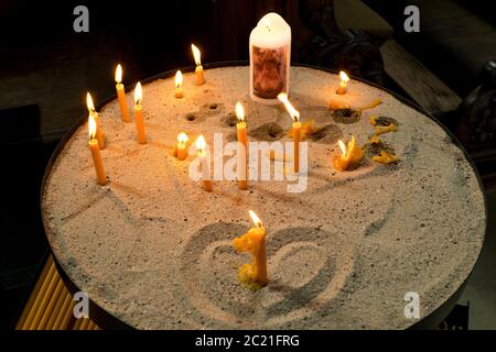 Candles burning in the church on sand with heart Stock Photo