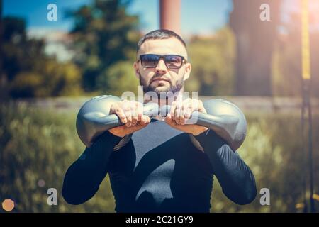 Shot of fit young man exercising with kettlebell outdoors in the park. Strong young guy training at park in morning. Stock Photo