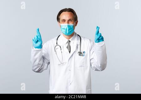 Covid-19, preventing virus, healthcare workers and vaccination concept. Optimistic doctor praying for patients lives, end of coronavirus, cross Stock Photo