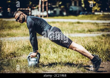 Attractive fitness instructor doing heavy weight exercise with kettlebell in the park. Fitness concept. Stock Photo