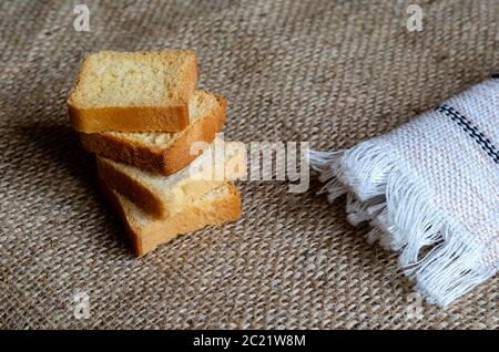 A stack of Four square toasts on burlap. Close-up of crunchy toasts next to a white linen towel. A fringed towel. Selective focus. Stock Photo