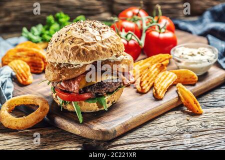 Beef budrger with double cheese, potato wedges, onion ring, tomato, mayonnaise on a dark chopping board Stock Photo