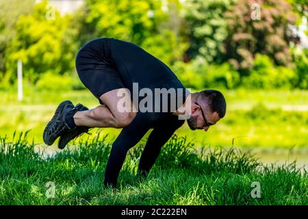 Handsome, muscular, strong man training near lake doing yoga. Concentrated adult sportsman doing push up exercises. Stock Photo