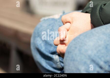 Closeup of a man's hands, selective focus on intertwined fingers and nails, arms and body are blurred. Action may show worry or depression.. Stock Photo