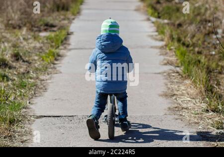 A boy rides a balance bike on the track. Spring mood. Sun. Stock Photo