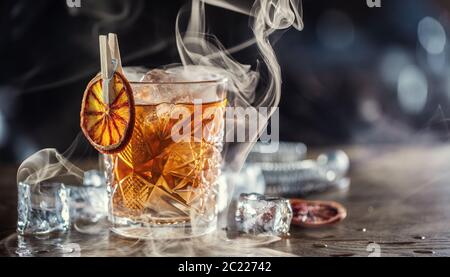 Smoked old fashioned rum cocktail with cubes of ice around on a dark background Stock Photo