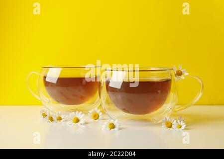 Cups of tea and chamomile on white table against yellow background Stock Photo