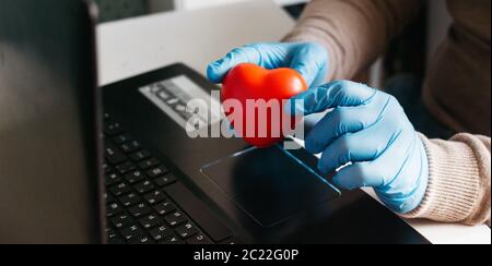 A man working from home on a laptop wearing disposable gloves for protection. Coronavirus outbreak. Quarantined business man. Work at home. Stay at Stock Photo