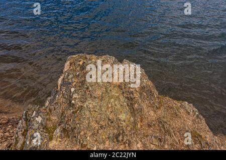 Big brown rock on beach of a mountain lake and blue wavy water on a summer day. Travel, tourism, and resort in nature concept Stock Photo