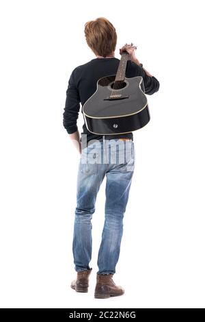 Back view of young rocker guitarist walking away carrying acoustic guitar on shoulder. Full body length isolated on white background. Stock Photo