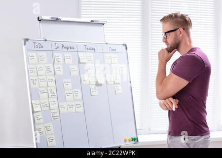 A Young Businessman Standing In Office Looking At Adhesive Notes On White Board Stock Photo