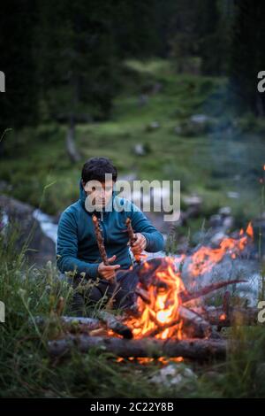 Young man making fire while camping outdoors, in an alpine wilderness Stock Photo