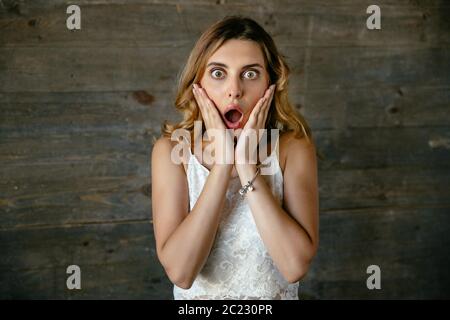 Surprised attractive young woman shocked about something, keeping mouth opened and holds hands near her face. Stock Photo