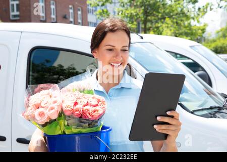Smiling Female Florist Carrying Bouquet In Blue Bucket Using Digital Tablet Stock Photo