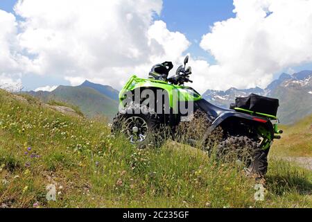 With the ATV in the mountains. A green ATV stands on a steep mountain path. Stock Photo