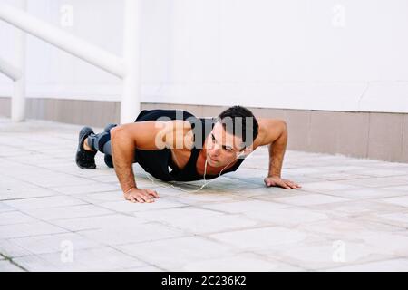 Attractive muscular guy doing push-ups exercises, during workout outdoors, listening to music in earphones. Stock Photo