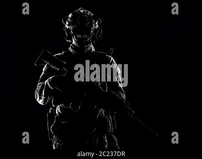 Low key studio portrait of army special forces elite soldier with hidden behind mask and glasses face, battle helmet, tactical radio headset, standing Stock Photo